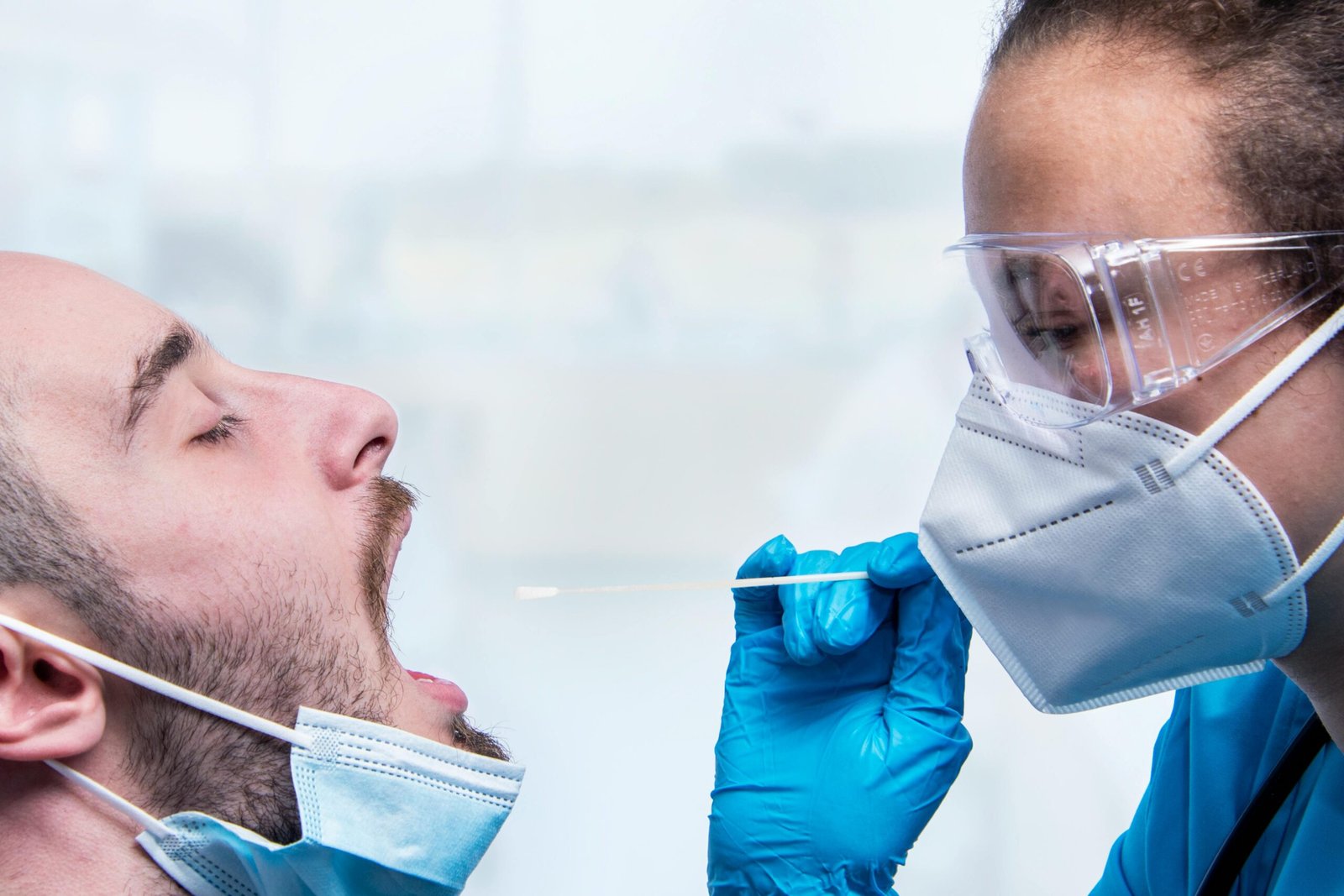 A healthcare worker conducts a COVID-19 swab test on a patient wearing masks.